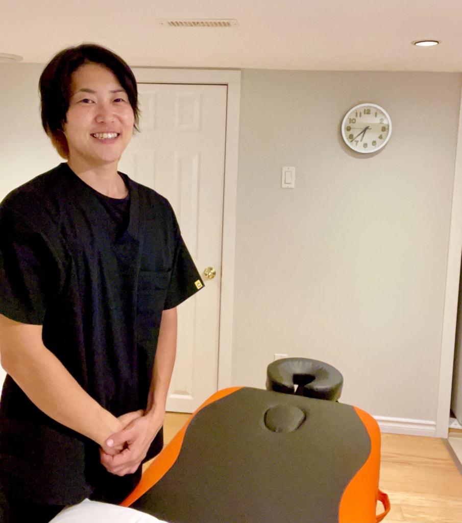 A student stands next to a massage therapy table