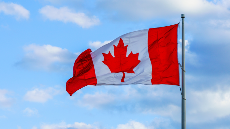 The Canadian Flag flies in the wind. The flag has a red maple leaf over a white center with the edges also colored red.
