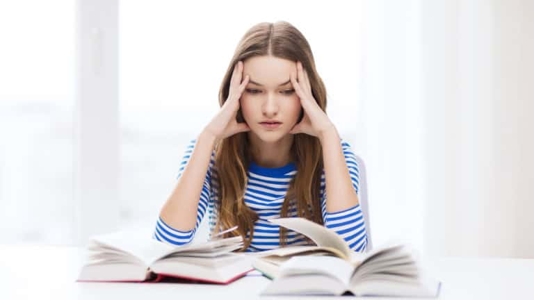 A person sitting at a desk with their head in their hands and a book in front of them.