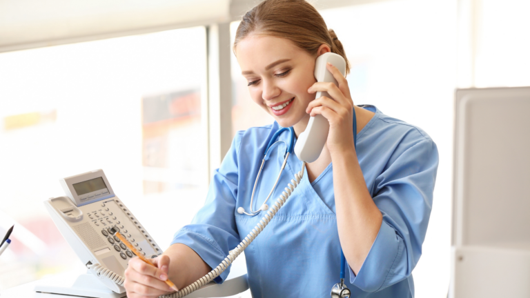 A smiling woman wearing scrubs talks on the phone and takes notes